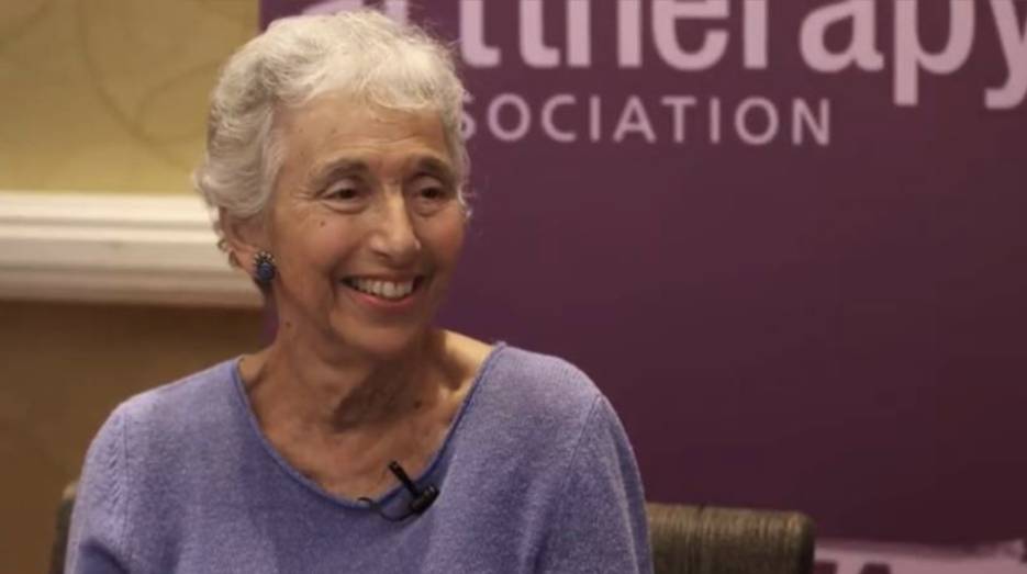 Portrait of Judy Rubin. She's smiling wearing a purple sweater. She has short white hair.